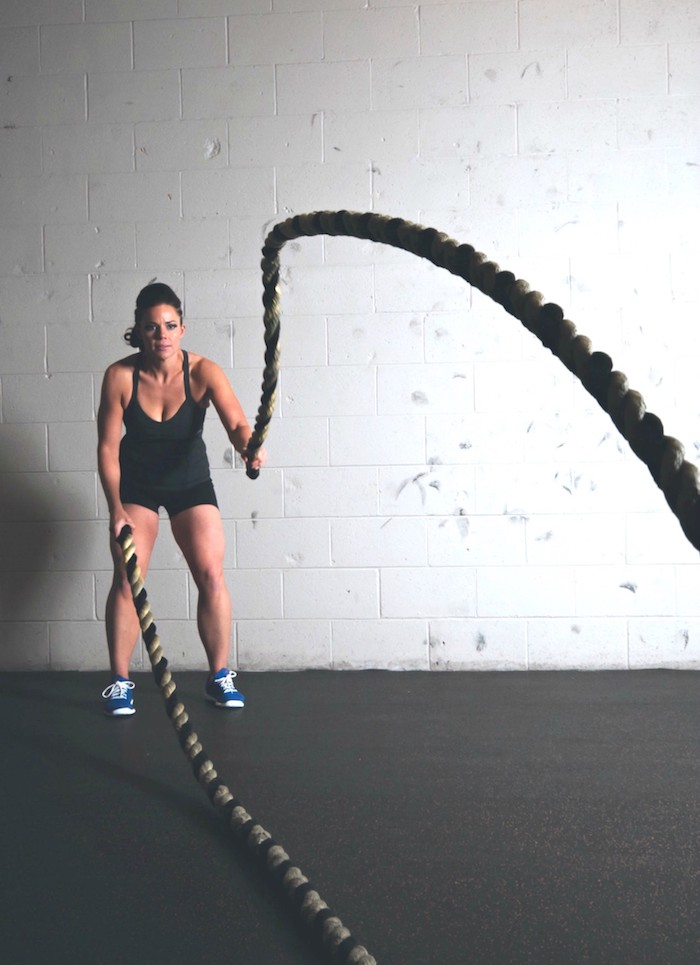 Woman in gym working out with ropes, performing a hiit workout routine