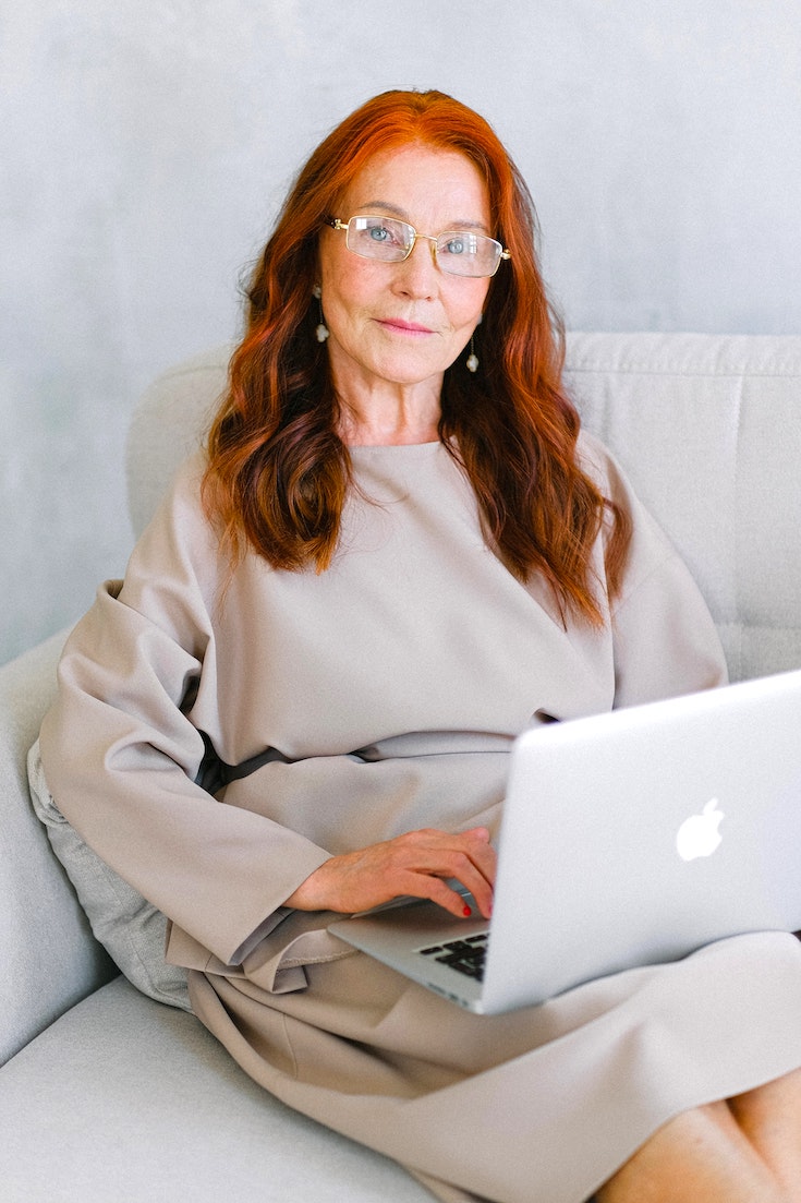 Elderly woman in neutral tone dress working on laptop