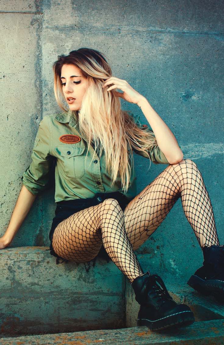 Woman in fishnets, black shorts and boots and green shirt