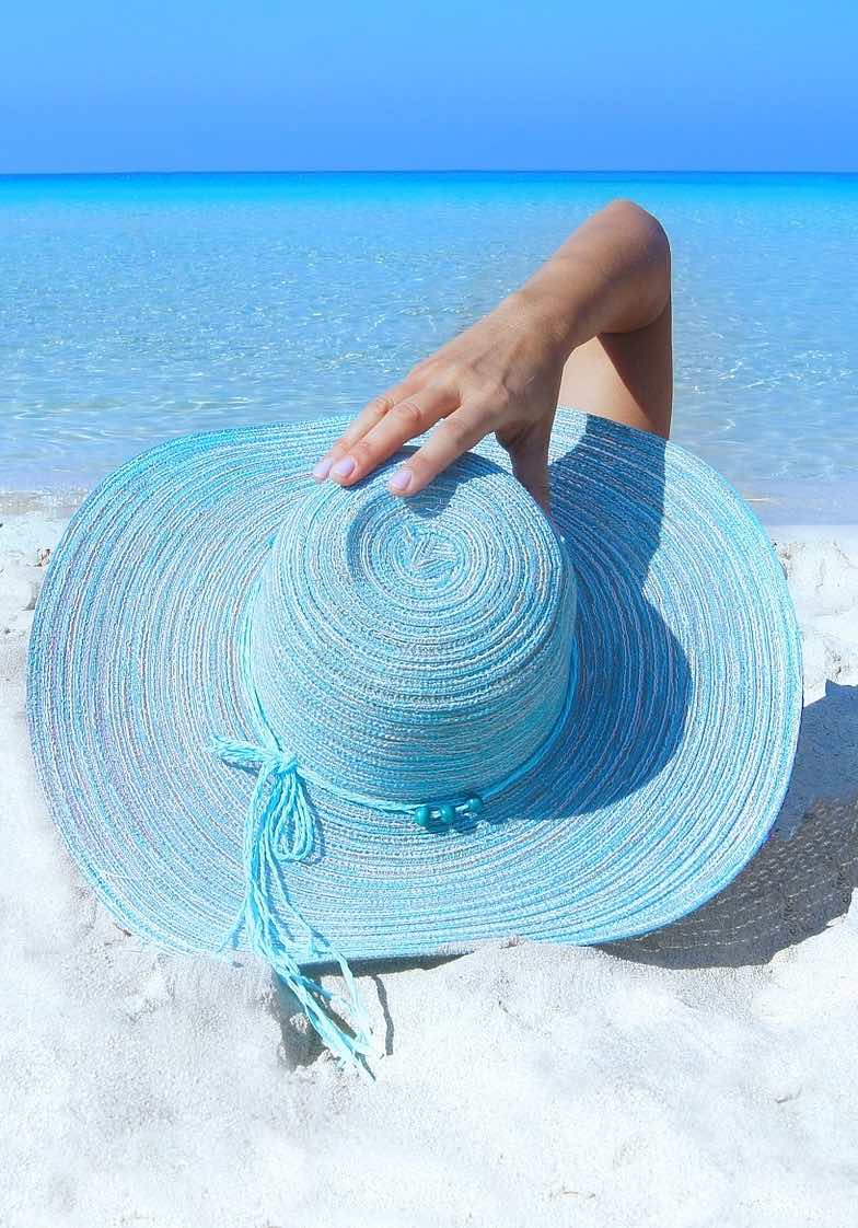 Woman on the beach with sun hat, cooling off from the heat